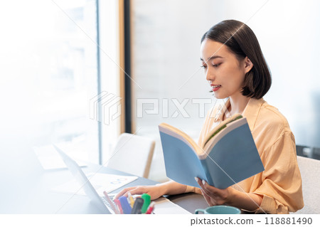 一位女士在電腦上工作，手裡拿著一本參考書 118881490