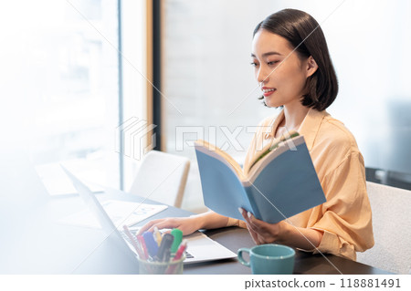 A woman working on a computer with a reference book in hand 118881491