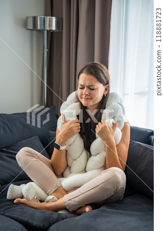 Young woman sits on a sofa with a weighted pillow on her shoulders and does a therapeutic practice aimed at getting rid of feelings of loneliness, session with a neurocoach 118881723