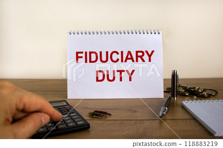 White note with inscription 'fiduciary duty' on beautiful wooden table, male hand on calculator, pen, paper clips, coins. Business concept. White background. 118883219