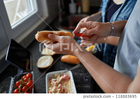 A pair of male hands slice a hot dog bun. A young couple cooks food together at home. A pair of male hands slice a hot dog bun. A young couple cooks food together at home. 118883695