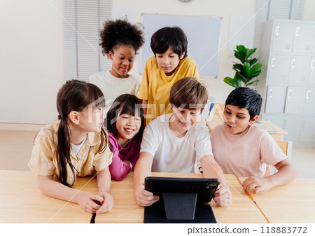 Diverse elementary students collaborate on digital tablet in modern classroom. Multicultural group engages in interactive learning, showcasing inclusive education and technological integration Diverse elementary students collaborate on digital tablet in modern classroom. Multicultural group engages in interactive learning, showcasing inclusive education and technological integration 118883772
