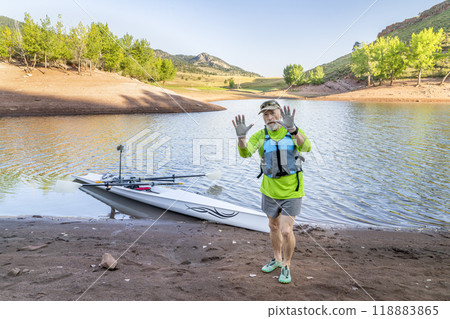 senior rower wearing life jacket and rowing gloves on a shore of Horsetooth Reservoir in northern Colorado senior rower wearing life jacket and rowing gloves on a shore of Horsetooth Reservoir in northern Colorado 118883865