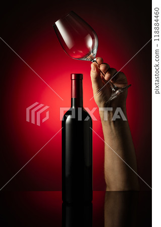 Unopened bottle of red wine and hand with wine glass. 118884460