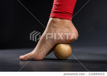 Myofascial release of foot muscles with wooden yoga massage ball on dark background, close-up Myofascial release of foot muscles with wooden yoga massage ball on dark background, close-up 118884810