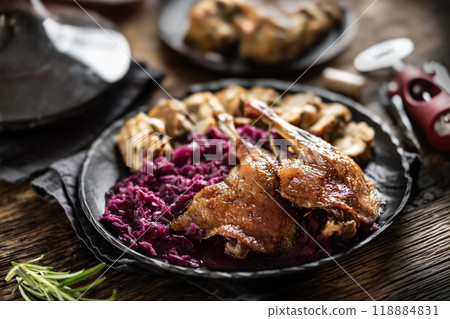 Portion of roast duck leg red cabbage homemade dumplings on plate and red wine on the background 118884831