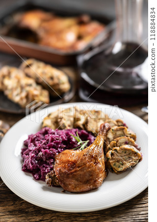 Portion of roast duck leg red cabbage homemade dumplings on plate and red wine on the background Portion of roast duck leg red cabbage homemade dumplings on plate and red wine on the background 118884834