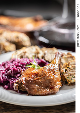 Portion of roast duck leg red cabbage homemade dumplings on plate and red wine on the background Portion of roast duck leg red cabbage homemade dumplings on plate and red wine on the background 118884835