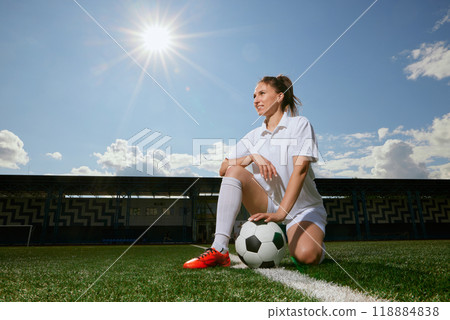 girl Football player in white shorts and red boots sets a soccer ball on a green field 118884838