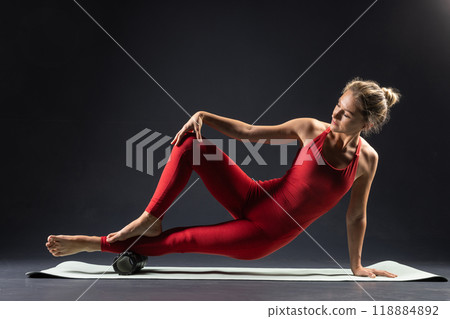 physiotherapy massage, woman with yoga roller on floor for leg tension on dark background 118884892