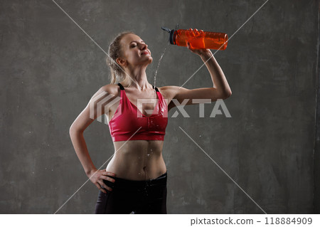 sporty woman pouring water from bottle on herself after workout on grey background. sport concept 118884909