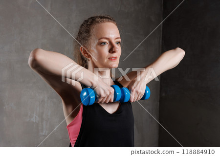 A woman exercises with blue dumbbells in a fitness studio. She performs a strength exercise A woman exercises with blue dumbbells in a fitness studio. She performs a strength exercise 118884910