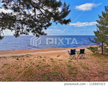 Sunny beach day with two camping chairs overlooking a calm lake under a clear blue sky 118885423