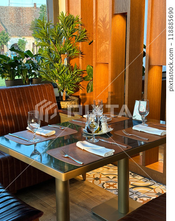 Cozy restaurant interior with elegantly set table, ready for guests. the warmth of the wooden accents and green plants create a welcoming atmosphere. Cozy restaurant interior with elegantly set table, ready for guests. the warmth of the wooden accents and green plants create a welcoming atmosphere. 118885690