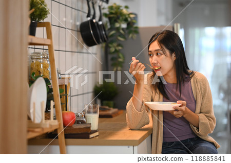 Young woman enjoying a meal, sitting kitchen counter. Everyday lifestyle and healthy eating concept 118885841