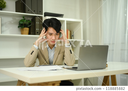 Stressed businessman holding head in his hands in front of laptop and financial reports 118885882