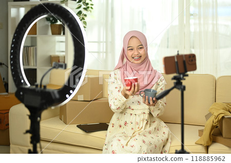 Happy young Muslim woman live streaming and presenting ceramics products to her audience. E-commerce concept 118885962