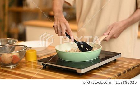 Close up of man using a spatula to stir and cook the ingredients in frying pan on an induction stove 118886029