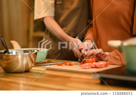 Young couple cutting tomatoes on a wooden cutting board, preparing spaghetti bolognese in kitchen Young couple cutting tomatoes on a wooden cutting board, preparing spaghetti bolognese in kitchen 118886051