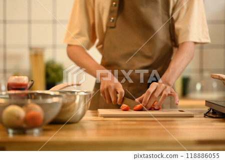 Young man preparing healthy meal, cutting tomatoes on a wooden cutting board Young man preparing healthy meal, cutting tomatoes on a wooden cutting board 118886055