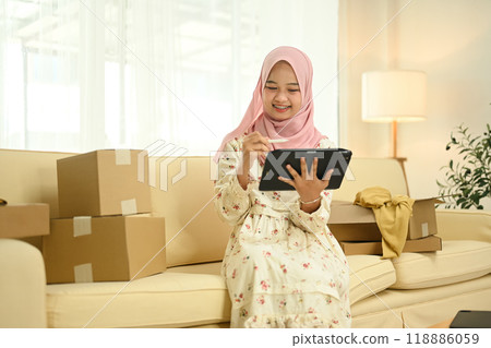 Smiling young Muslim woman managing her online store working on digital tablet at home office 118886059