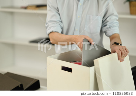 Young male office worker packing belongings in box after being fired Young male office worker packing belongings in box after being fired 118886088
