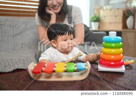 Adorable toddler boy playing with colorful toys while mother lovingly watches. Childhood and nurturing care concept 118886090