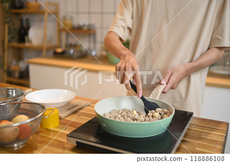 Close up shot of man stirring ingredients in frying pan with wooden spatula Close up shot of man stirring ingredients in frying pan with wooden spatula 118886108