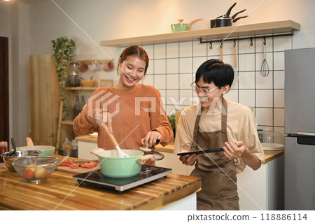Cheerful young couple preparing a delicious meal and following an online recipe on digital tablet 118886114