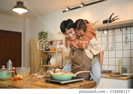 Joyful young couple wearing aprons cooking in a cozy kitchen. Relationships, cooking and happy domestic life 118886117