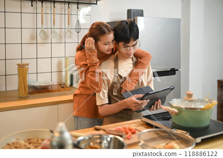 Sweet moment of young couple looking at a recipe on digital tablet while cooking together in kitchen 118886122