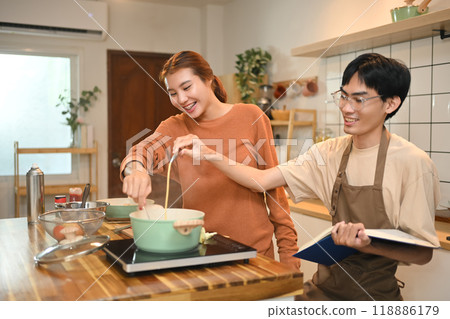 Young couple enjoying time together while preparing meal in a cozy kitchen. Relationships and domestic life concept Young couple enjoying time together while preparing meal in a cozy kitchen. Relationships and domestic life concept 118886179