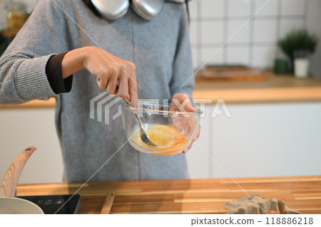 Cropped shot of woman beating eggs in a bow with fork, preparing breakfast in the kitchen 118886218