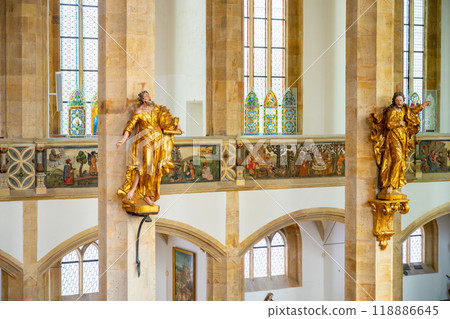 The interior showcases stunning late Gothic architecture, featuring golden statues and intricate stained glass. Visitors admire the serene atmosphere and detailed artwork throughout the church. 118886645