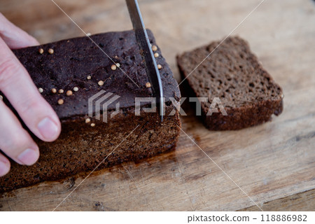The man cuts whole-wheat rye bread on a wooden cutting board. The man cuts whole-wheat rye bread on a wooden cutting board. 118886982