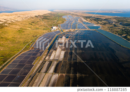 Aerial view of salt pans under the sun showcasing seawater evaporation for salt production. Aerial view of salt pans under the sun showcasing seawater evaporation for salt production. 118887285