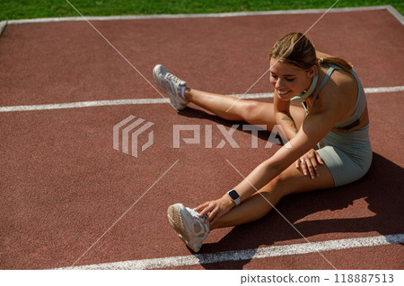 An athletic woman is stretching on the track field to prepare for her warmup exercises 118887513