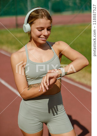 An active woman is running outdoors, equipped with headphones and a smartwatch on her wrist 118887527