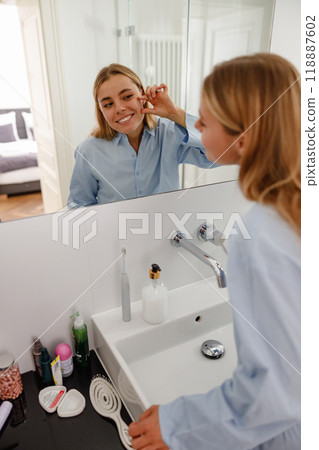 A Smiling Woman Happily Applying Skincare Products in Her Modern Bathroom Mirror Space 118887602