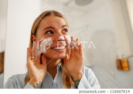 A Cheerful Woman Enjoying an Invigorating Skincare Routine in a Modern Bathroom Setting 118887614
