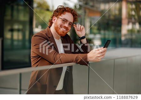 A Stylish Man with a Bright Smile, Happily Using His Smartphone While Outdoors in Nature 118887629