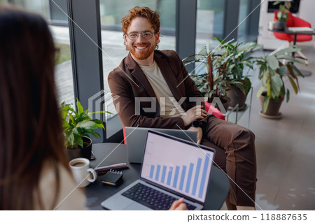 A Business Meeting Taking Place in a Modern Office Setting Featuring Charts and Indoor Plants 118887635