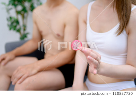 Young woman's hand holding a condom, male and female couple holding contraceptives, married couple, pregnancy, sexual consent 118887720