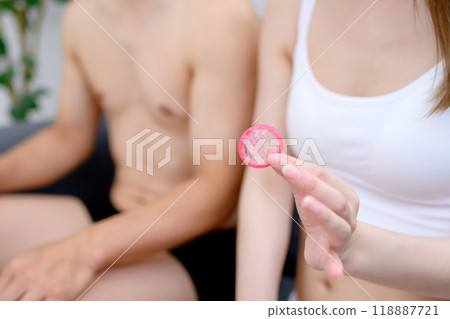 Young woman's hand holding a condom, male and female couple holding contraceptives, married couple, pregnancy, sexual consent 118887721