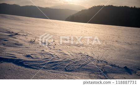 A serene winter landscape captures the beauty of freshly fallen snow. The distant mountains are silhouetted against the evening sky, showcasing soft hues as the sun sets, creating a peaceful 118887731