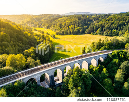 Aerial view of Sychrov Railway Bridge surrounded by lush greenery, showcasing its architectural structure against a vibrant landscape. Aerial view of Sychrov Railway Bridge surrounded by lush greenery, showcasing its architectural structure against a vibrant landscape. 118887761