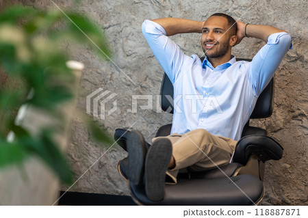 Smiling businessman sitting in chair with raised arms in office Smiling businessman sitting in chair with raised arms in office 118887871