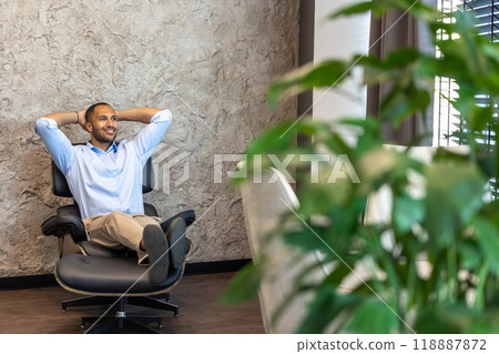 Smiling businessman sitting in chair with raised arms in office Smiling businessman sitting in chair with raised arms in office 118887872