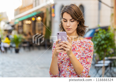 Smiling woman girl using smartphone typing text answering messages chatting online in city street 118888324