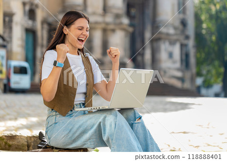 Overjoyed happy young woman working on laptop celebrating win good message news in city street 118888401